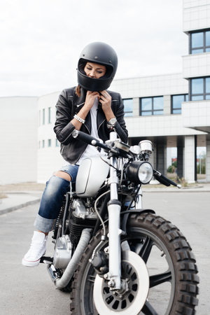 Outdoor lifestyle portrait of biker girl sits on vintage custom motorcycle and buttons helmetの写真素材