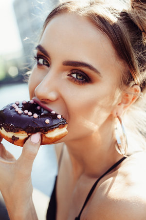 Outdoors lifestyle portrait of funny beautiful girl eating donutの写真素材