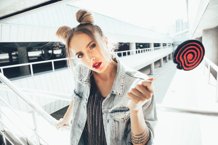 Young cheeky girl walking on the street holding a lollipop. Outdoors, lifestyle portrait