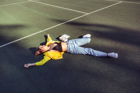 Outdoors lifestyle portrait of funny beautiful girl with a box of donuts lying on the tennis court