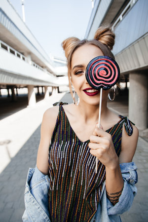 Young happy girl having fun with a lollipop. Outdoors, lifestyle portrait