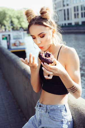 Portrait of funny beautiful girl eating donut. Hungry woman licking fingersの写真素材