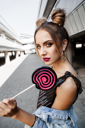 Young sexy woman walking on the street holding a lollipop. Outdoors, lifestyle portraitの写真素材