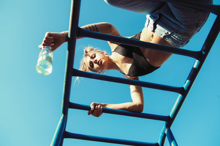 Active young woman exercising on ladder. Sporty fit girl working out at outdoor gym and drinking waterの写真素材