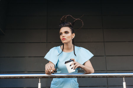 Beautiful young woman showing hot drink in disposable paper cup. Outdoors lifestyle portrait of girl