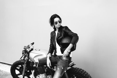 Outdoor lifestyle portrait of young biker woman sitting on a vintage custom motorcycleの写真素材