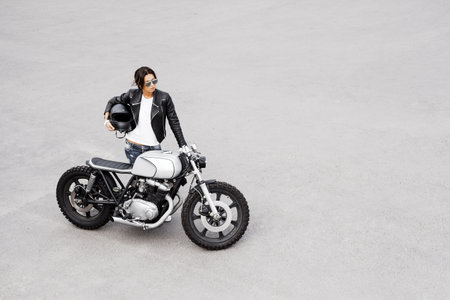 Outdoor lifestyle portrait of sexy biker girl wearing leather jacket and vintage custom motorcycle. Woman get to rideの写真素材