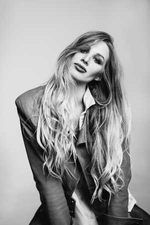 Pretty girl with long wavy hair . Fair-haired model with curly hairstyle and fashionable makeup . Female model over grey background. Black and white tonedの写真素材