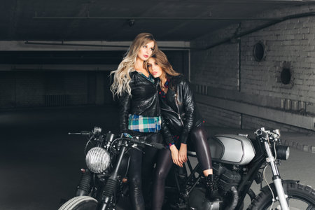 Sexy biker girls sitting on vintage custom motorcycles. Beautiful women with Healthy Long Hair ringlets wearing stylish leather jacketsの写真素材
