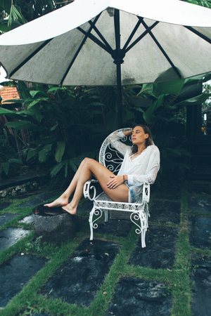 Woman relaxing at gorgeous pool side of luxury tropical villa in rainy dayの写真素材