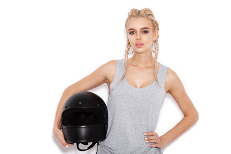 Woman with two braids holding mitorbike helmet. Expressive girl in a gray T-shirt on white background not isolatedの写真素材