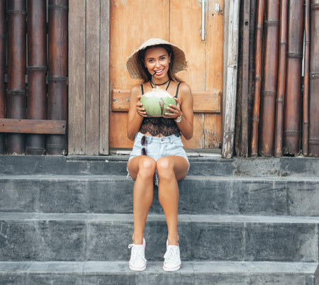 Portrait of attractive young woman drinking coconut juice. Happy girl relaxing on summer vacationの写真素材