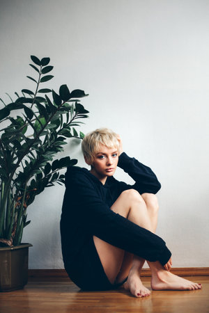 young woman in black hoodie while looking into camera and a pot plant next to herの写真素材