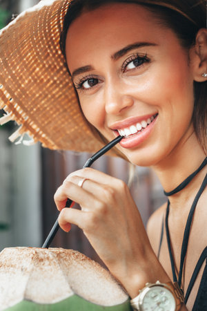 Close-up of attractive young woman drinking coconut juice. Happy girl relaxing on summer vacationの写真素材