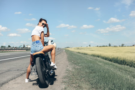 The girl sitting on a motorcycle near the road.の写真素材