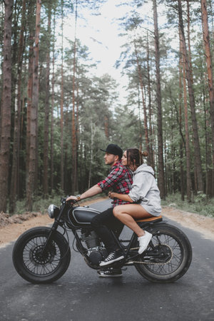 Young Caucasian couple on a motorcycle caferacer on the forest road.の写真素材