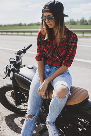 The girl sitting on a motorcycle near the road.の写真素材