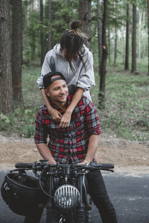 Young Caucasian couple on a motorcycle caferacer on the forest road.の写真素材