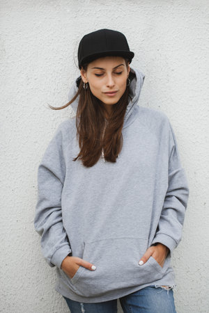 Young girl wearing blank and oversize long hoodie and black cap. Outdoors lifestyle portraitの写真素材