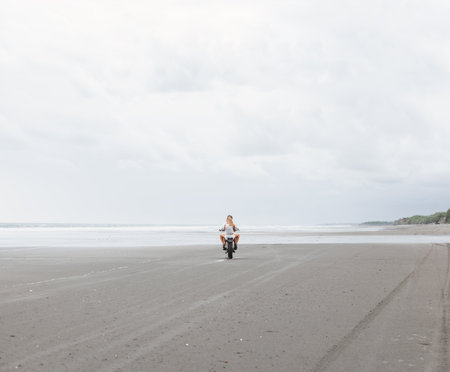 Young beautiful couple hipsters riding retro motorcycle on the beach, outdoor portrait, posing, in jeans shorts and t-shirts, bearded guy, blonde girl, travel together, ocean, seaの写真素材