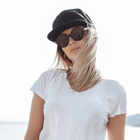 Close-up of young sexy swag girl. Outdoor lifestyle portrait of female in sunglasses and black cap. Summer photo toned style Instagram filtersの写真素材