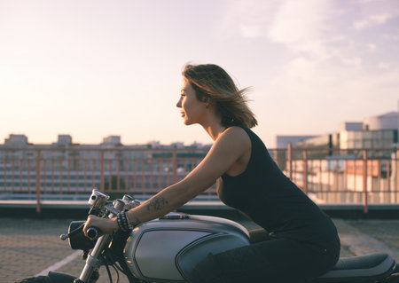 Biker woman ridding custom cafe racer motorcycle on empty city road at sunsetの写真素材