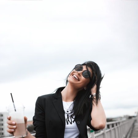 Portrait of beautiful brunette girl walking down the street. Keeping takeaway drink in hand. Smiling. Urban city scene. Outdoorsの写真素材
