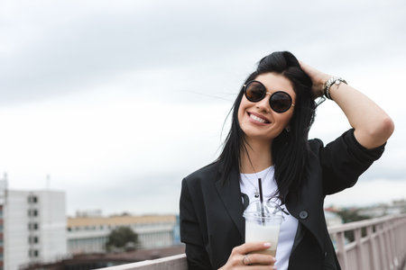 Portrait of beautiful brunette girl walking down the street. Keeping takeaway drink in hand. Smiling. Urban city scene. Outdoorsの写真素材