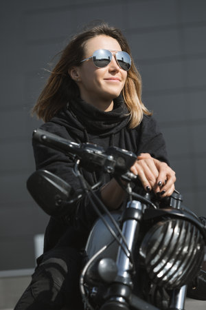 Outdoor lifestyle portrait of young biker woman sitting on a vintage custom motorcycleの写真素材