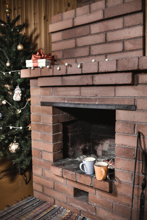 Christmas tree with decorations standing at a fireplace with a garland, gift and two cups with tea on itの写真素材