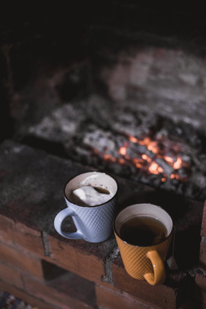 Two cups of tea with marshmallow against the background of defocused smoldering coals in a fireplace, top viewの写真素材