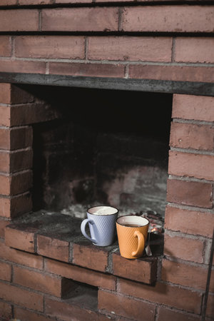Two cups of tea stand on a fireplace against the background of the burning-down coalsの写真素材