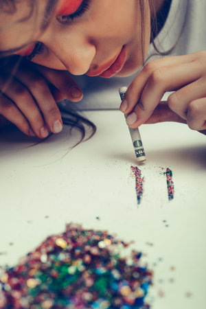 swag sexy girl is sniffing shining colorful glitter (imitation cocaine) on the white table. Oange hadows makeup. Conceptual art shootの写真素材