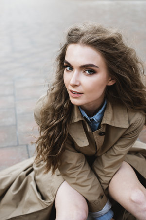 attractive curly smiling woman sitting on the stairs outdoors wearing cloakの写真素材