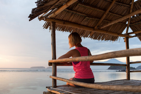 young sporty woman or girl silhouette (back view) watching sunset, looking at sea or ocean, sky, chilling in summerの写真素材