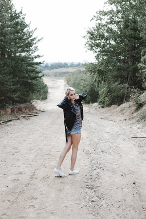Young pretty stylish girl in black leather jacket posing, walking outdoors.の写真素材