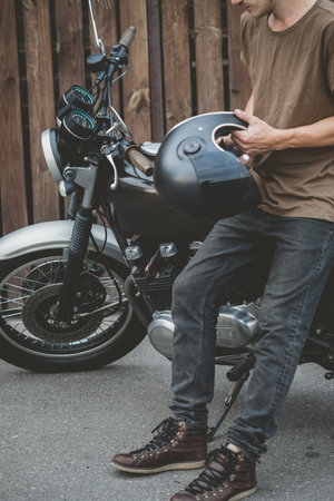 Handsome rider biker guy wearing black helmet and sitting on classic style cafe racer motorcycle....