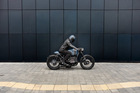 Biker man with Black blue rebuilt vintage custom motorcycle cafe racer in front of wallの写真素材