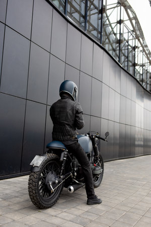 Biker man with Black blue rebuilt vintage custom motorcycle cafe racer in front of wall