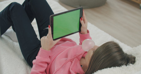 View over head on of caucasian woman lying on the bed at home. Girl holding tablet computer with green screen while watching something. Chroma key.の写真素材