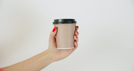 Mockup of female hand holding coffee brown paper cup on light white wall backgroundの写真素材
