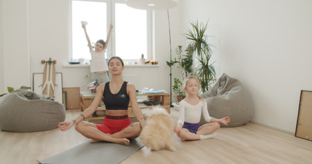 Mother meditating with daughter while active energetic child son playing, calm young mom doing yoga exercise at home for stress relief relaxing with naughty little kid.の写真素材