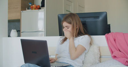 Sick woman using laptop computer and doing meeting or web conference from home. Freelance female model working out of office. Girl sitting on bed. Self isolationの写真素材