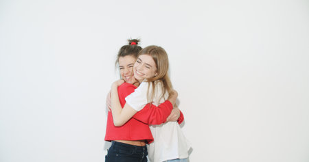 Two smiling crazy girl in summer clothes hug. Young women dancing . Models posing on white wall...