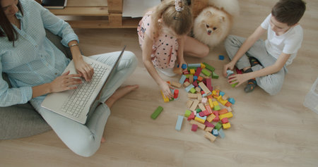 Happy mom and cute kids sitting at home, mother with little children playing with toys . Young woman works from home. Self-isolationの写真素材