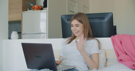 Attractive woman using laptop computer and doing meeting or web conference from home. Freelance female model working out of office. Girl sitting on bed. Self isolationの写真素材