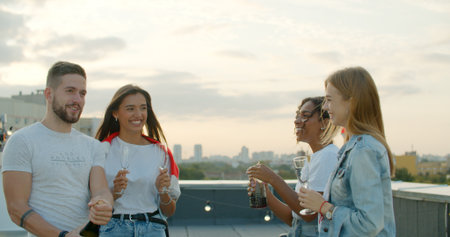 Man opening bottle of champagne with female friends. Group of happy young people laughing, having fun. celebrating birthday at party on rooftopの写真素材