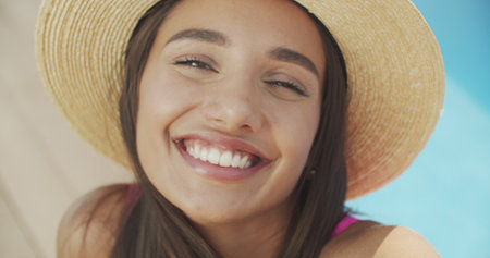 Young woman, making selfie, smiling, funny face, posing at pool at sunny summer day, stylish hatの写真素材