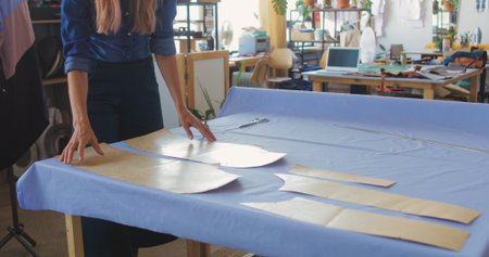 Young woman cutting fabric by edge of paper pattern while making new item for seasonal fashion collectionの写真素材