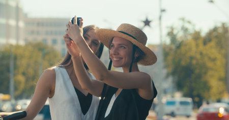 Two women making selfie. Lifestyle and health in city. Girls riding vintage bike and electric scooter on urban background.の写真素材